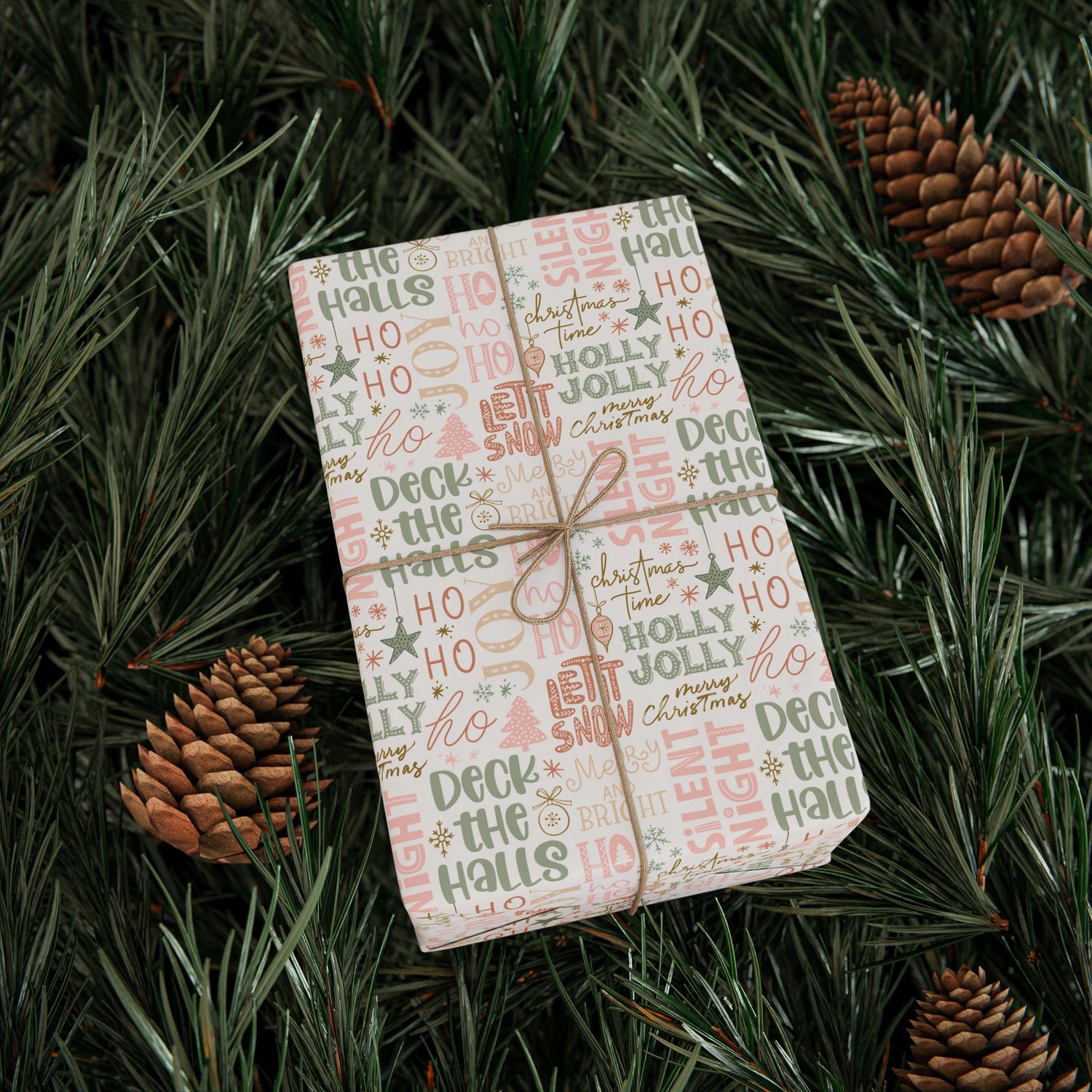 Gift wrapped in Christmas-themed paper on a bed of pine needles with pine cones.