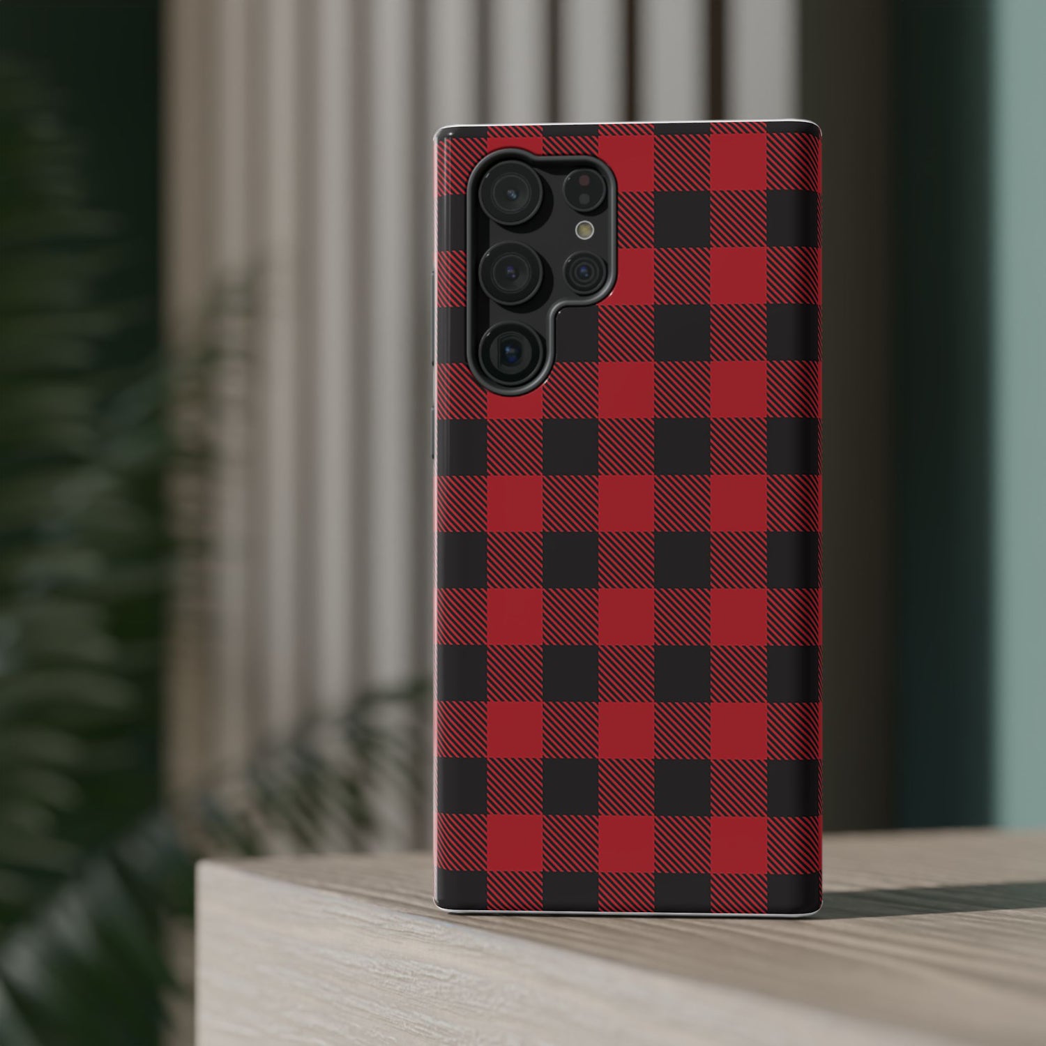 A red and black checkered phone case with a camera module on the back, placed on a wooden surface with a blurred background.
