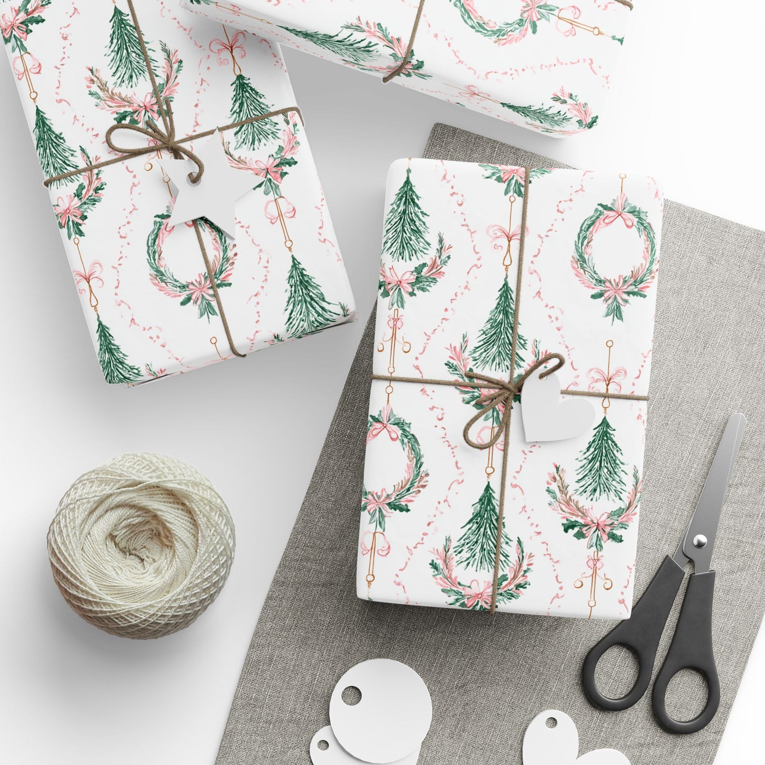 Gift boxes wrapped in festive paper with decorative ribbons, scissors, and twine on a neutral background.