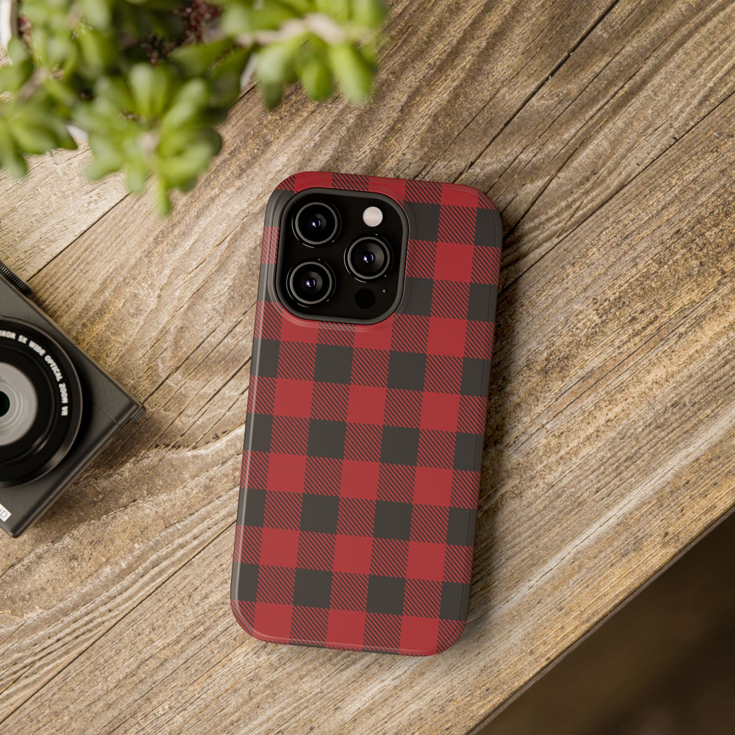 A red and black checkered phone case with a camera module on top, placed on a wooden surface next to a camera.