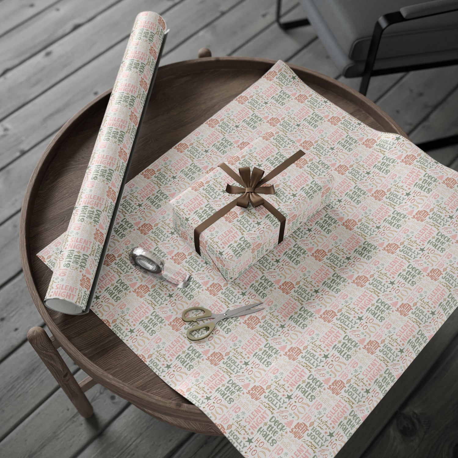 Gift wrapping paper with a roll, scissors, and a wrapped gift on a wooden table.