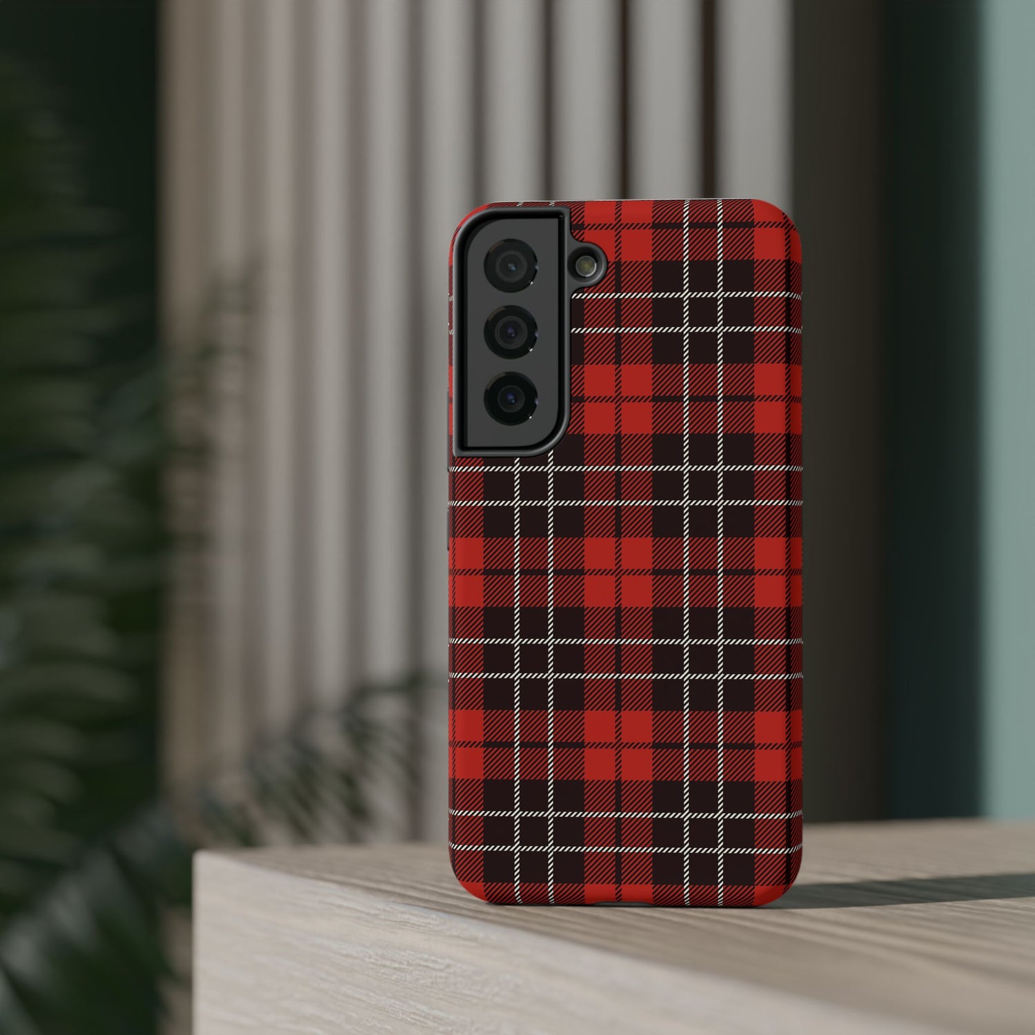 A red and black checkered phone case with a camera module on the back, placed on a wooden surface with a blurred background.