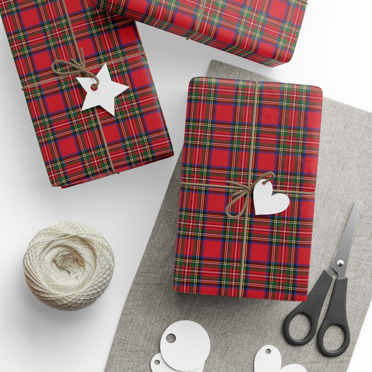 Red plaid gift wrap with decorative tags and scissors on a white surface