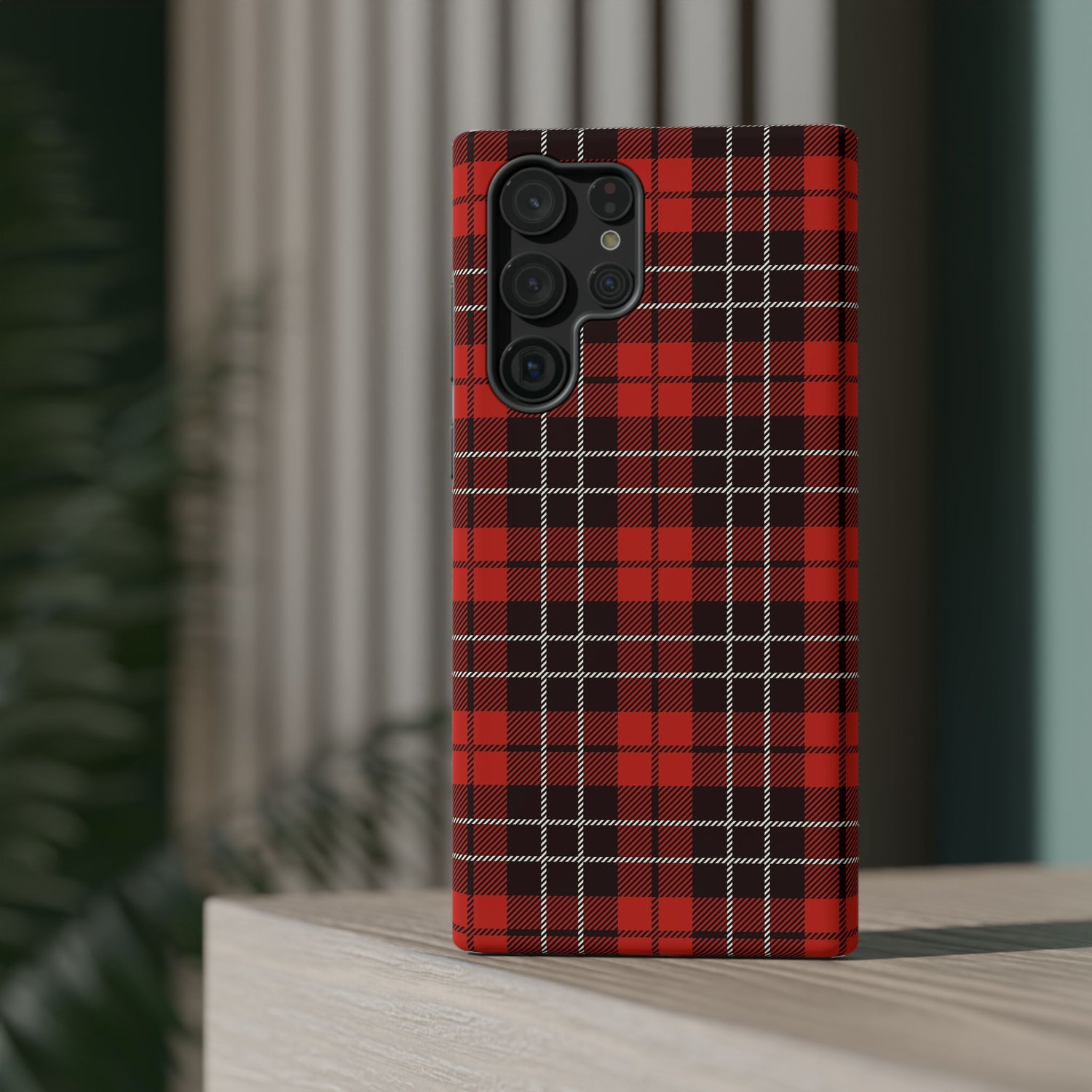 A red and black checkered phone case with a camera module on the back, placed on a wooden surface with a blurred background.