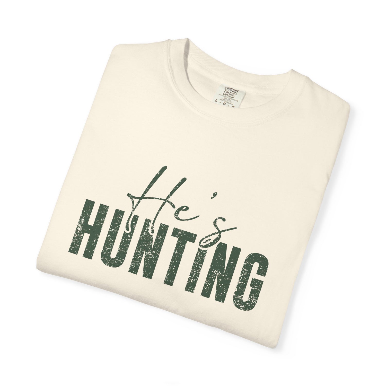 Folded cream-colored t-shirt with 'He's Hunting' text in green on a white background
