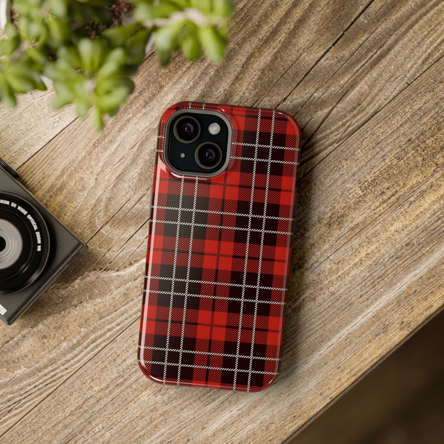 A red and black checkered phone case with a camera module on the back, placed on a wooden surface next to a small camera.